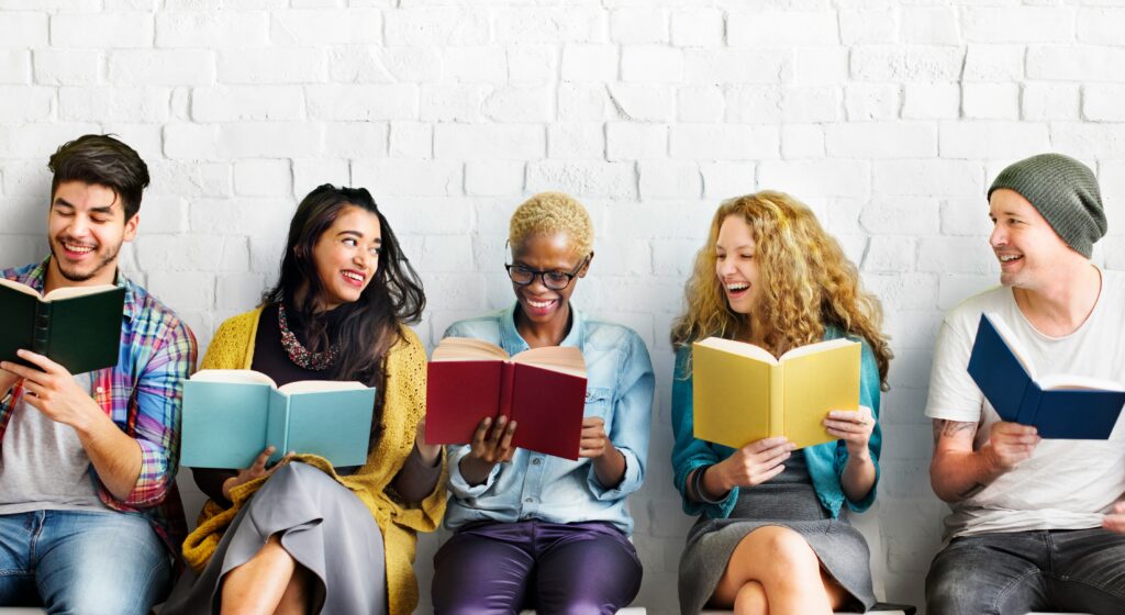 Grupo de estudiantes universitarios compartiendo y leyendo libros en una biblioteca.