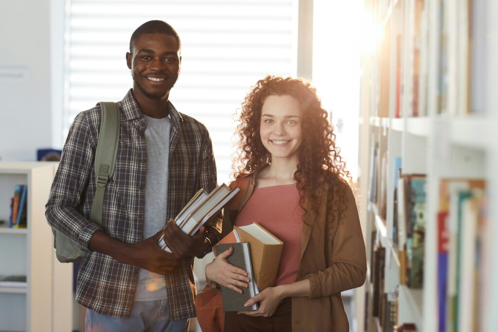 Dos estudiantes universitarios sosteniendo libros en una biblioteca, enfocados en la investigación y el aprendizaje.