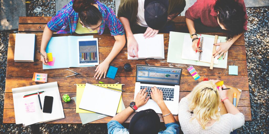 Varios estudiantes concentrados en una mesa de biblioteca analizando libros y documentos juntos.