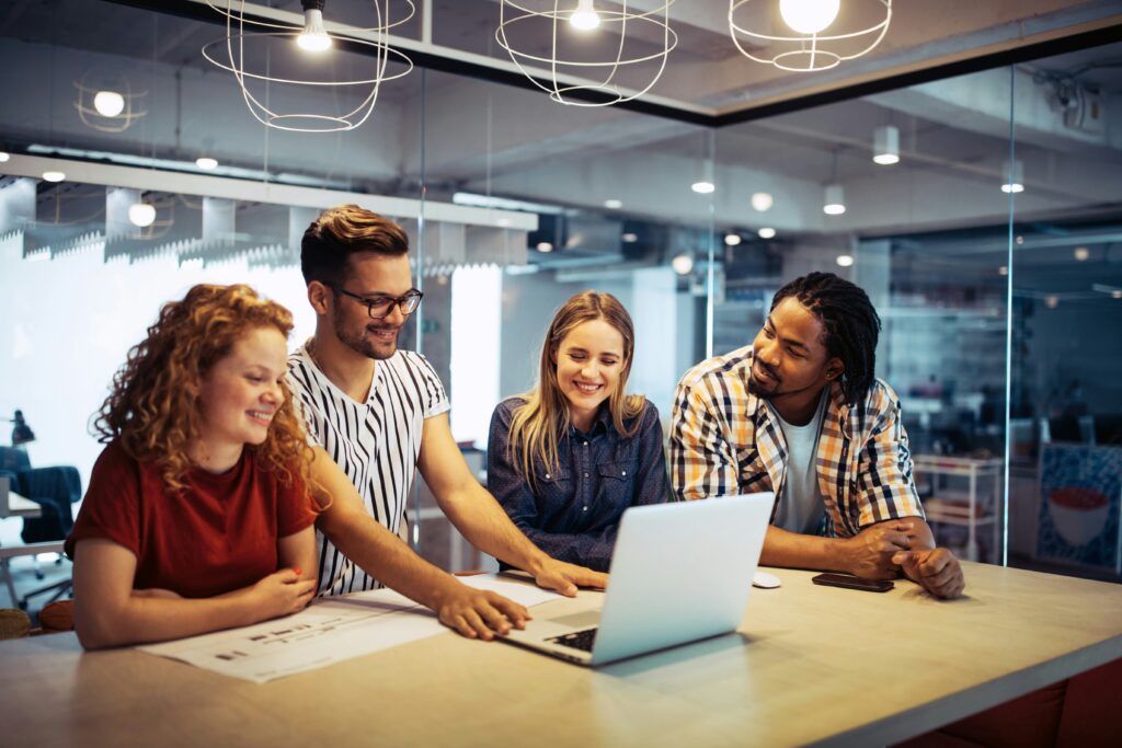 Cuatro estudiantes sentados juntos analizando información en una laptop y debatiendo ideas para un proyecto académico.