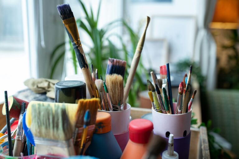 Primer plano de un conjunto de pinceles de diferentes tamaños y formas, con las cerdas teñidas de pintura, sumergidos juntos en un frasco en un taller de arte.