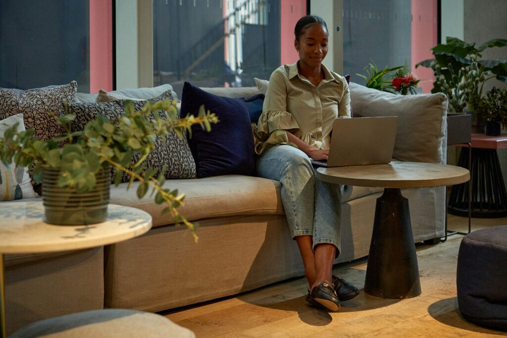 Una mujer joven sentada en un café moderno con una laptop abierta, mientras toma notas, simbolizando la lluvia de ideas y el pensamiento creativo digital.