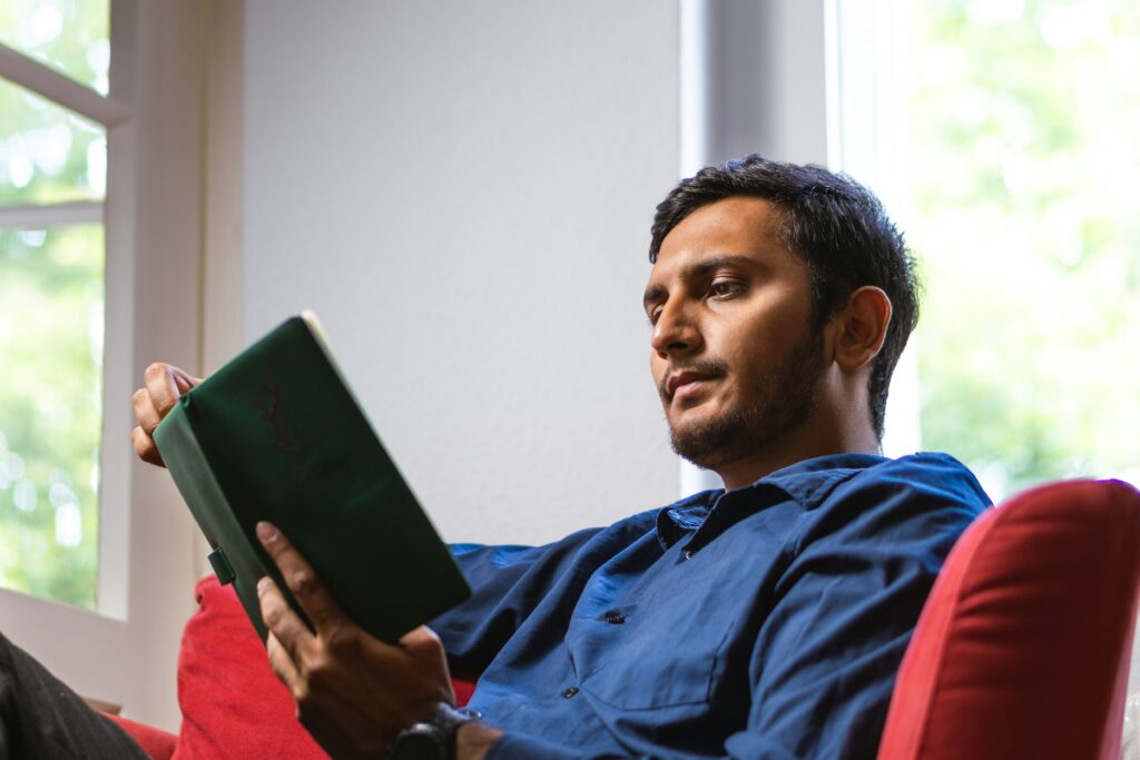Un hombre joven sentado revisando con atención un plan de estudios detallado escrito a mano en un cuaderno.