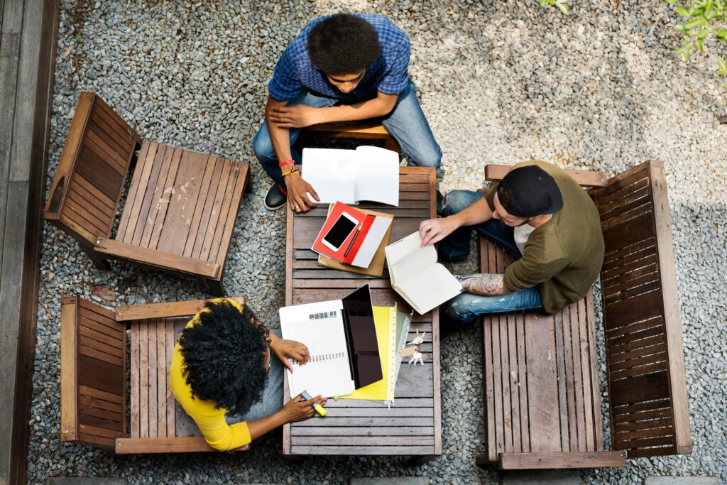 Tres personas sentadas alrededor de una mesa compartiendo ideas y escribiendo notas en cuadernos.