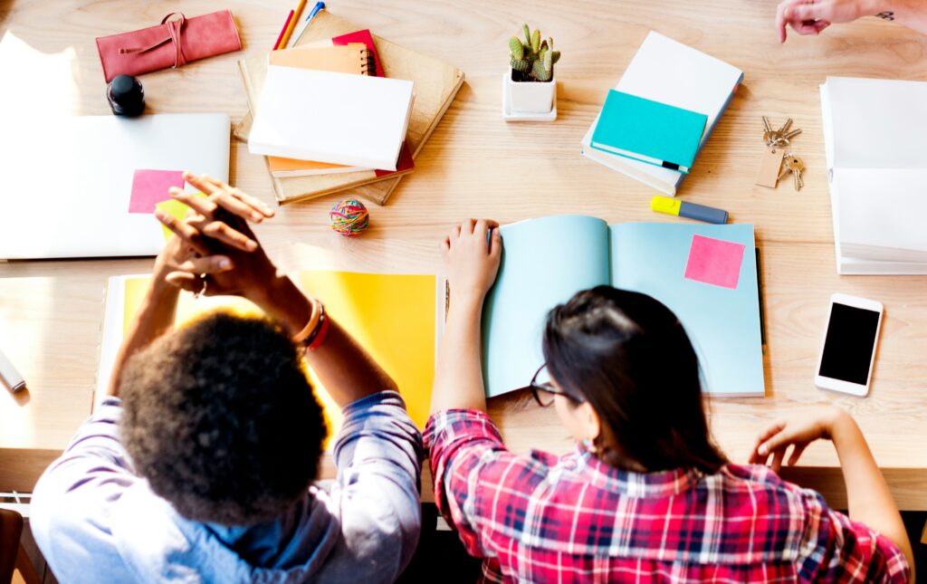Dos estudiantes jóvenes sentados a una mesa de madera consultando libros en una biblioteca.