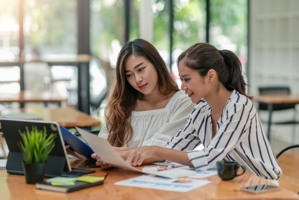 Dos compañeras de estudio concentradas analizando juntas el contenido de un libro de texto sobre una mesa de madera.
