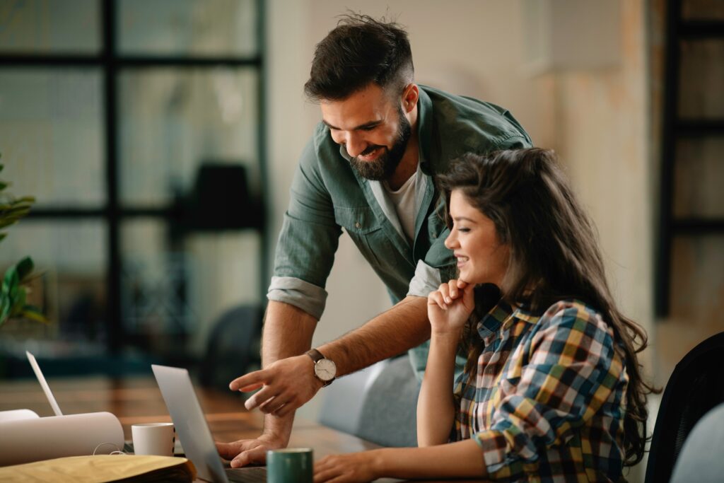 Dos profesionales colaborando en una computadora para aplicar soluciones técnicas de intraemprendimiento en la oficina.