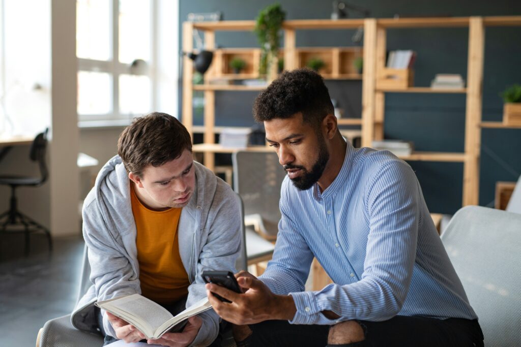 Dos estudiantes sentados a una mesa compartiendo materiales y libros mientras estudian en conjunto de forma organizada.