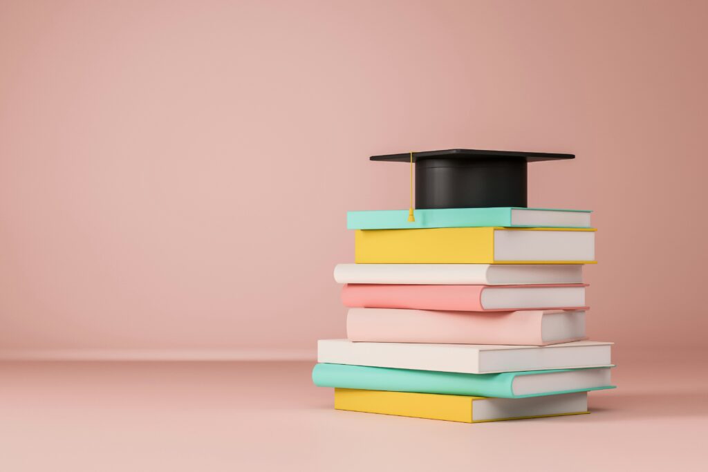 Sombrero de graduado colocado encima de varios manuales de estudio, simbolizando la culminación de los estudios superiores.