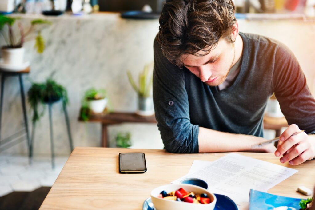 Hombre concentrado escribiendo una lista de tareas pendientes en su agenda para organizar su día y evitar la procrastinación.