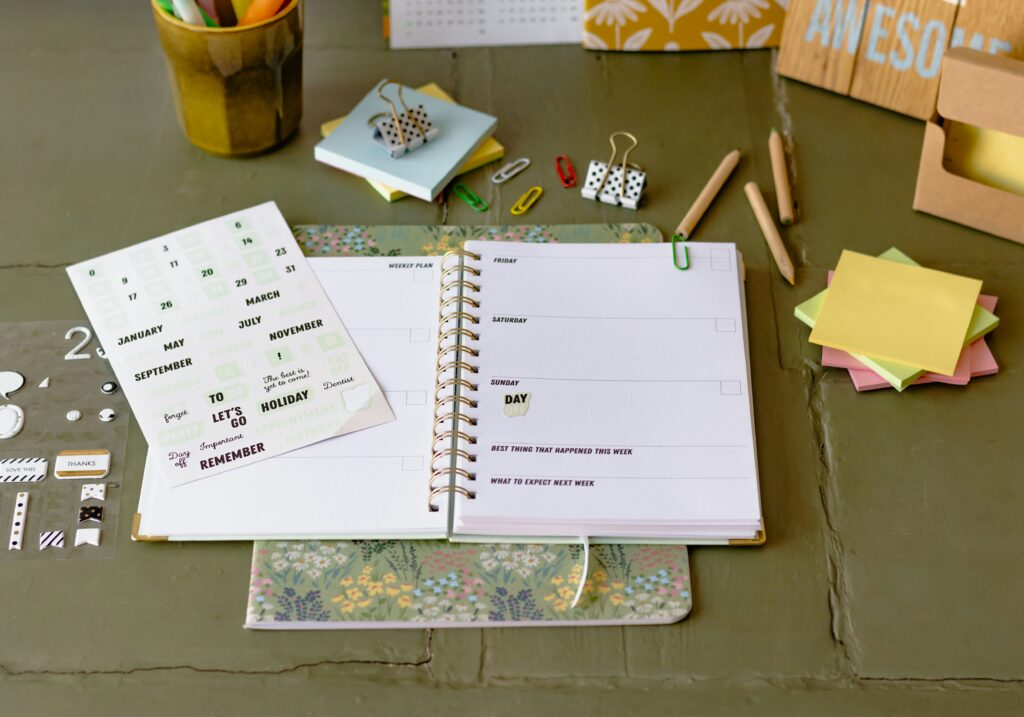 Una agenda abierta sobre una mesa de trabajo al lado de notas adhesivas de colores y bolígrafos, lista para la organización diaria.